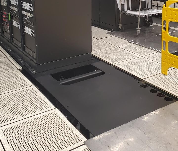 Welded steel mounting plate at the base of a power cabinet on a raised access floor in a data center